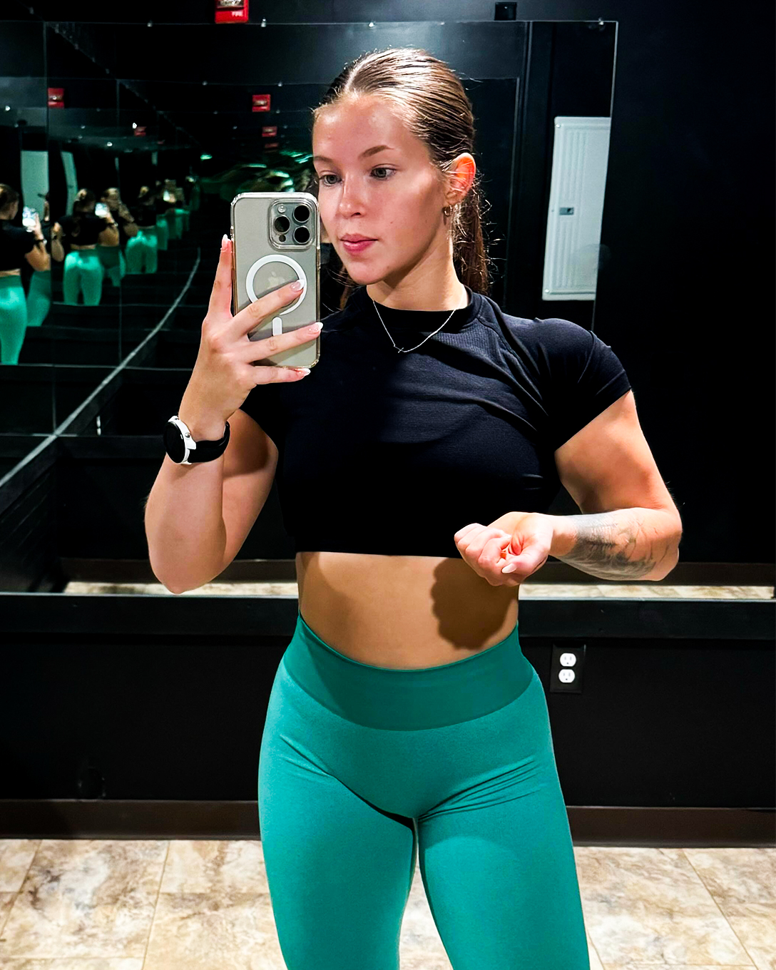 Emily, a NASM CPT and UESCA running coach, posing in a fitness room mirror after a workout. She is confident and showcasing her athletic physique.